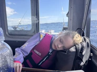 A young girl resting inside the boat, wearing a life jacket, while enjoying a day on the water.