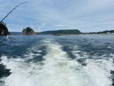 A scenic view from the boat showing the coastline and rocky formations, typical of a Pacific Northwest fishing environment.