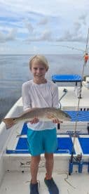 A young angler proudly displaying a Redfish on a fishing boat, showcasing a successful catch during a day on the water.