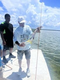 An angler proudly displaying a large fish while fishing from a boat in a scenic coastal environment.