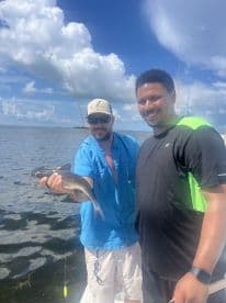 Two anglers proudly displaying a caught catfish while fishing on a sunny day in a coastal waterway.