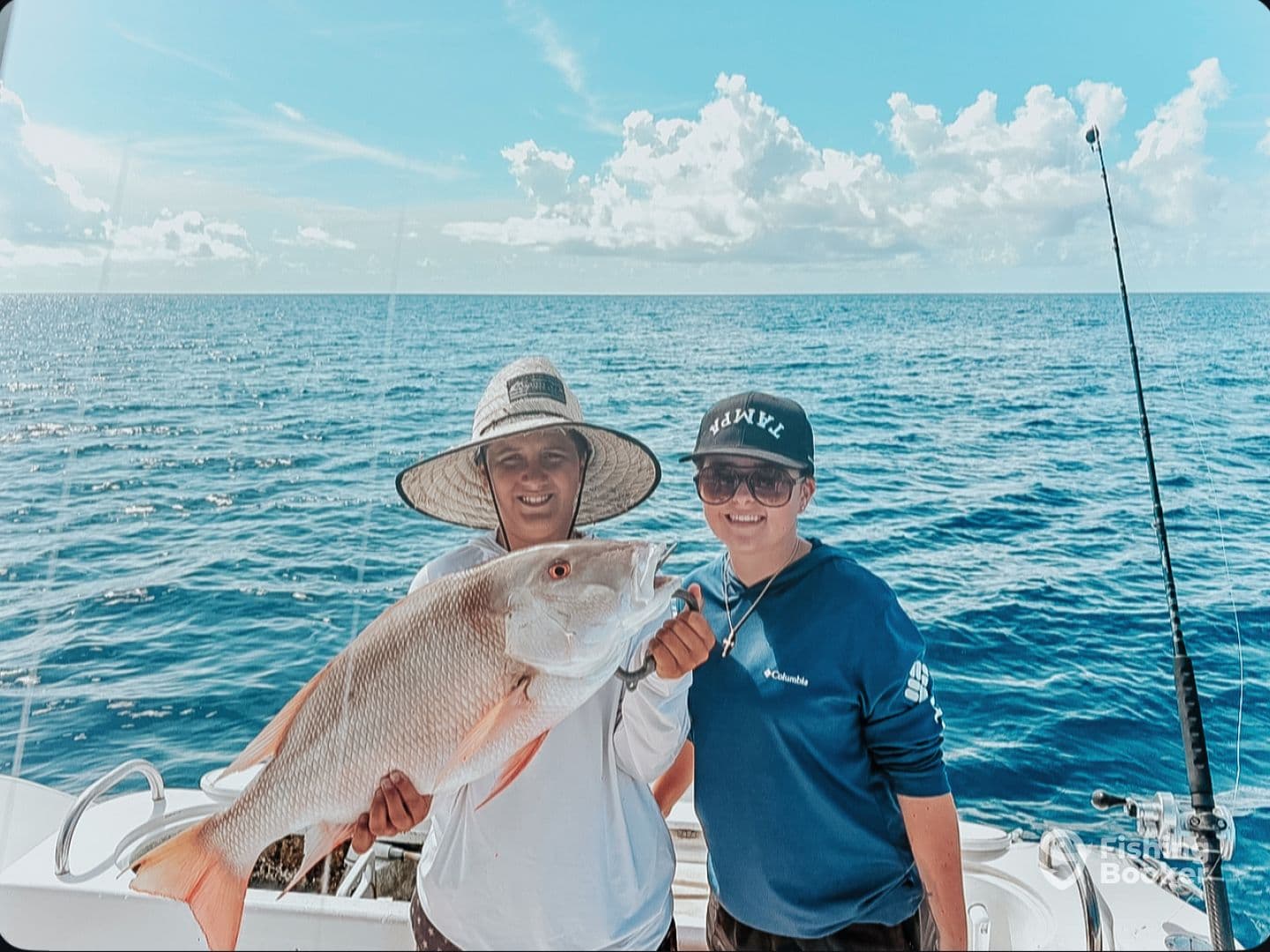 Two anglers proudly displaying a large Snapper while fishing on a sunny day in open waters.