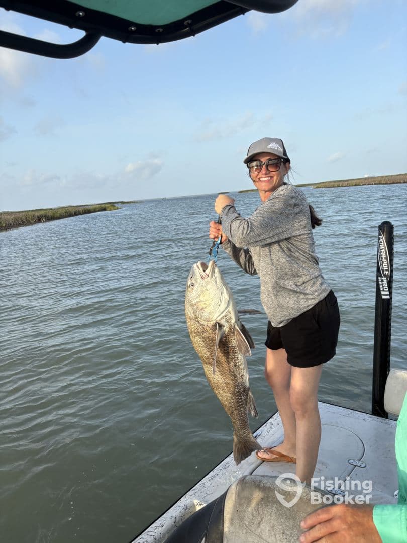 An angler proudly displaying a large Black Drum while fishing from a boat in a coastal waterway.