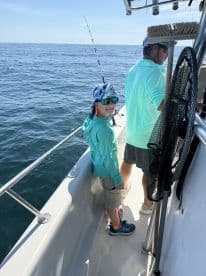 A young angler smiles while fishing on a boat, enjoying a sunny day on the water.