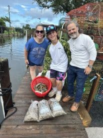 A family proudly displaying their catch of crabs and shrimp on a dock after a successful fishing trip.
