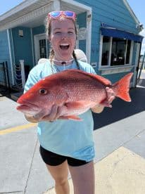 A proud angler holding a large Red Snapper in front of a colorful fishing shop, showcasing a successful day on the water.