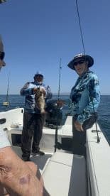 Two anglers aboard a boat, one proudly displaying a large Grouper caught during a fishing trip.