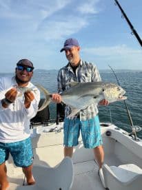 Two anglers proudly displaying their catch, a large Jack Crevalle, while fishing on a boat in a scenic coastal environment.