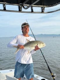 A young angler proudly displaying a large Jack Crevalle while fishing from a boat in calm waters.