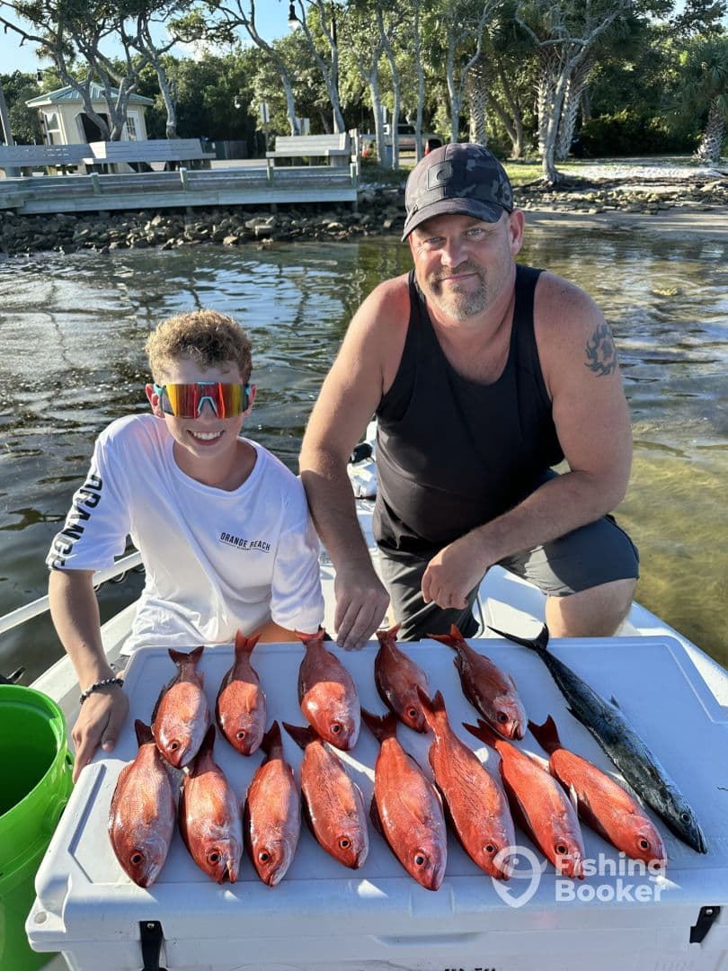 A young angler and an adult proudly displaying a catch of red snapper and a mackerel on a cooler after a successful fishing trip.