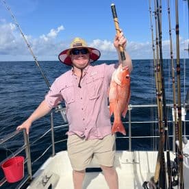 An angler proudly displaying a large Red Snapper while fishing offshore, showcasing a sunny day on the water.