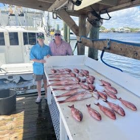 A young angler and an adult proudly pose beside a catch of multiple Red Snapper displayed on a cleaning table at the dock.