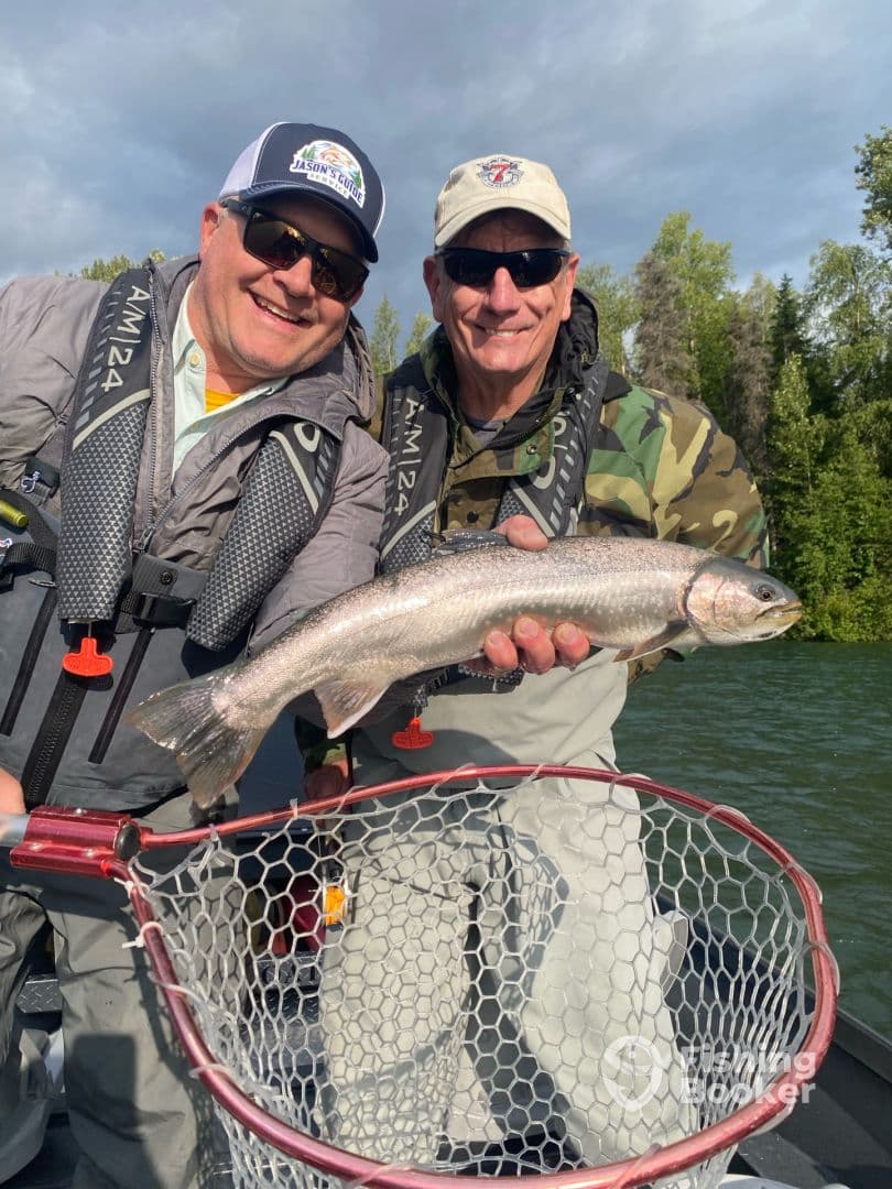 Two anglers proudly displaying a freshly caught Rainbow Trout while fishing in a scenic lake environment.