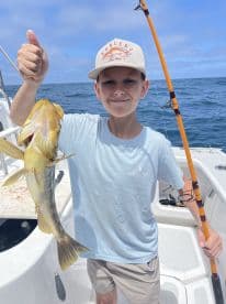 A young angler proudly displaying a caught fish while fishing on a boat, showcasing a sunny day on the water.