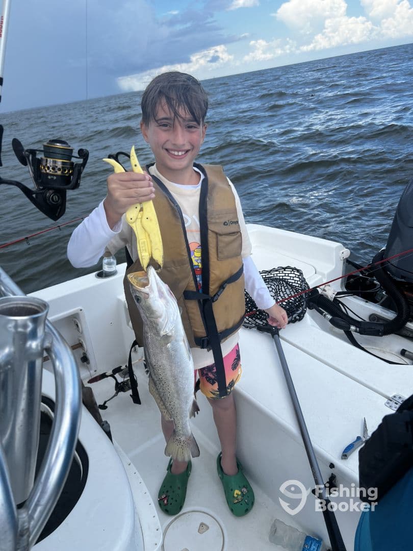 A young angler proudly displaying a Speckled Trout while fishing on a boat, showcasing a fun day on the water.