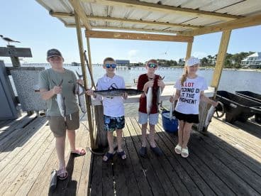 A group of young anglers proudly displaying their catch of Spanish Mackerel at the dock, enjoying a sunny day on the water.