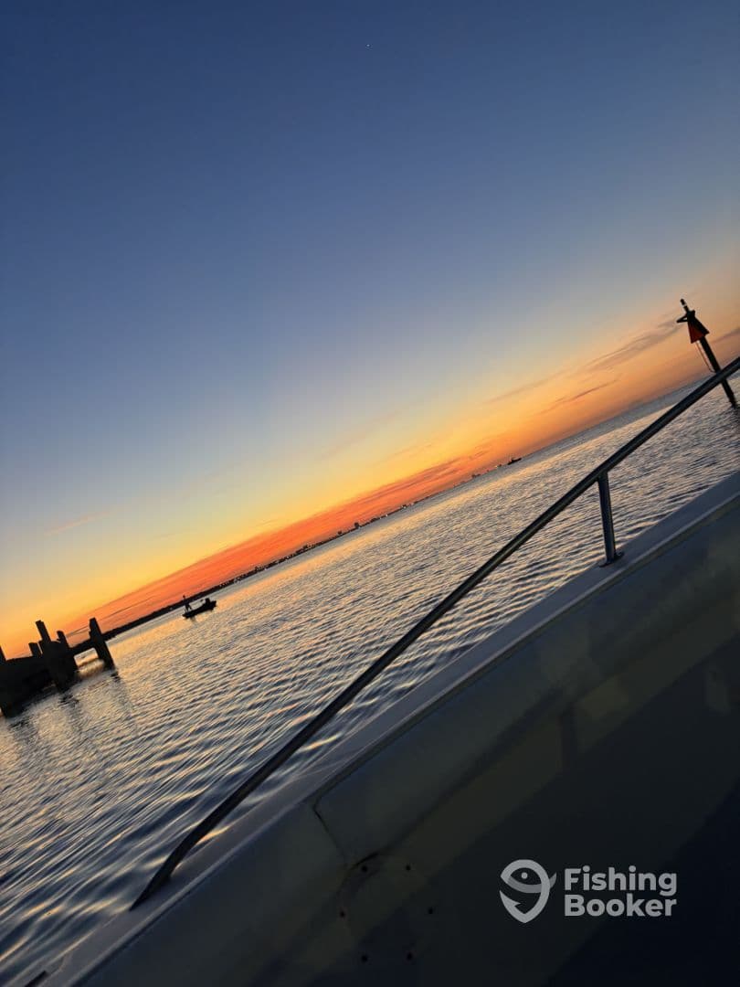 A serene sunset view from the side of a boat, showcasing calm waters and distant fishing boats in the background.
