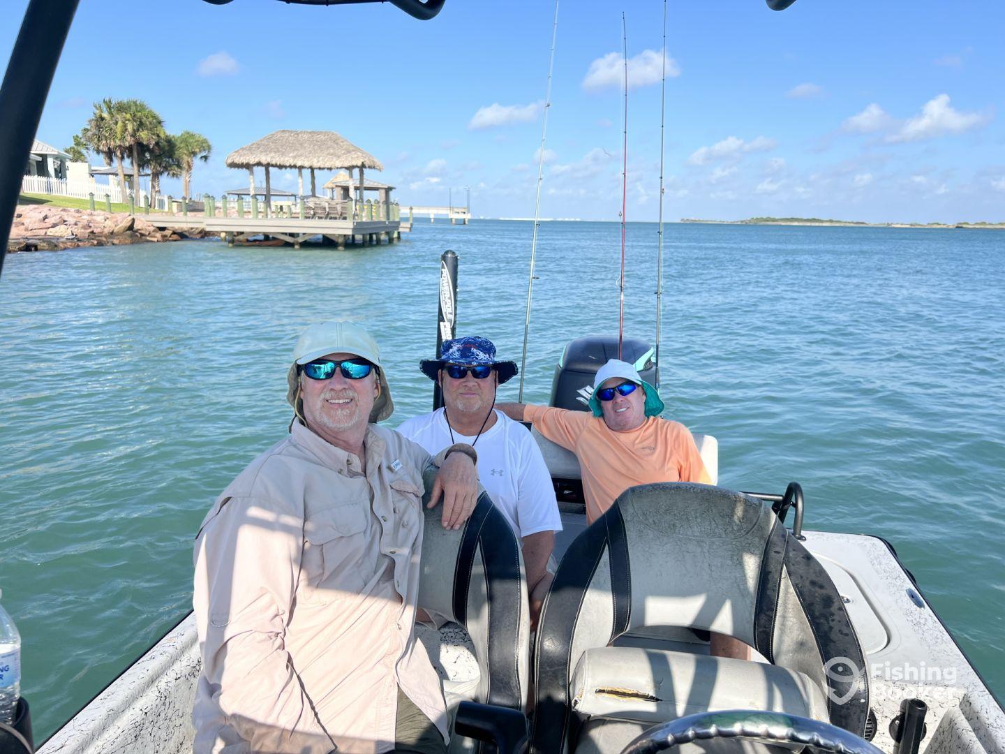 Three anglers relaxing inside a fishing boat, enjoying a sunny day on the water with a scenic view of the shoreline.