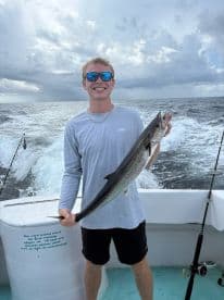 A young angler proudly displaying a large King Mackerel while fishing offshore, with a dramatic sky in the background.