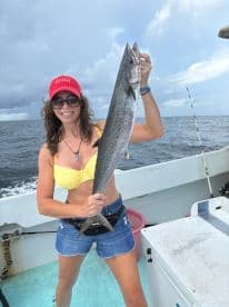 Angler proudly displaying a large King Mackerel while fishing offshore, showcasing a sunny day on the water.