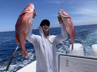 Angler joyfully displaying two large Red Snapper while fishing offshore, showcasing a successful day on the water.