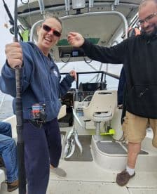 Two anglers aboard a boat, one holding a catch of multiple fish while the other assists, showcasing a lively fishing experience.
