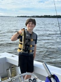 A young angler proudly displaying a caught fish while fishing on a boat in a scenic waterway.