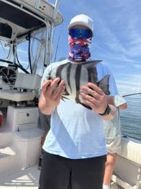 An angler proudly displaying a striped fish aboard a boat, showcasing a successful day on the water.