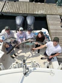 A group of anglers proudly displaying their catch of striped bass on a fishing charter, showcasing a fun family outing on the water.