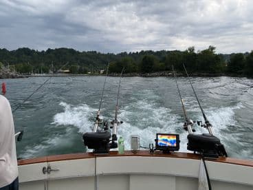 View from the helm of a fishing boat, showcasing fishing rods and electronics as it navigates through calm waters.