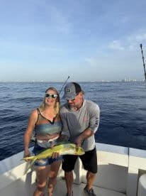 Two anglers proudly displaying a vibrant Mahi Mahi on a fishing charter in open waters.