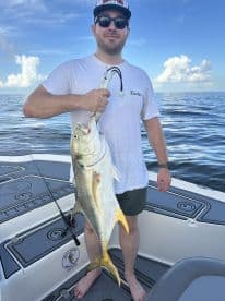 An angler proudly displaying a large Jack Crevalle while fishing on a boat in open waters.