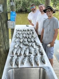 A group of anglers proudly displaying their catch of numerous Speckled Trout on a cleaning table at a fishing dock.