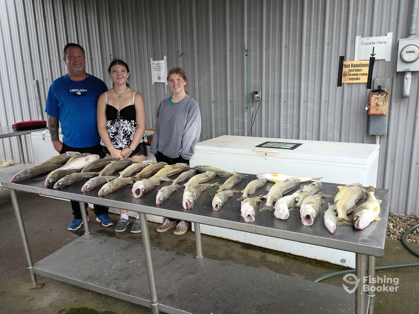 A family poses proudly with their catch of multiple Walleye displayed on a cleaning station after a successful fishing trip.