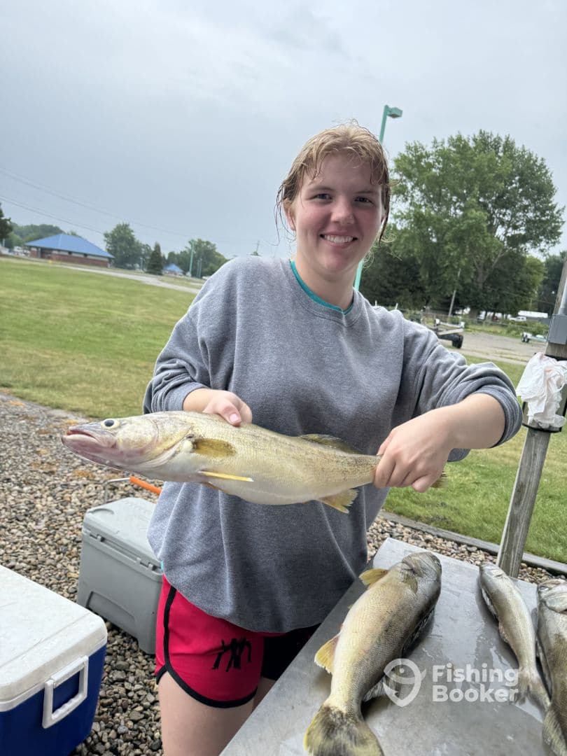 A young angler proudly displaying a Walleye after a successful fishing trip, with additional fish laid out on a table.