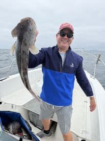 An angler proudly displaying a large Halibut aboard a fishing boat in open waters.