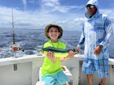 A young angler proudly displaying a vibrant Mahi Mahi while fishing on a charter boat in open waters.
