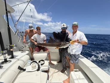 Group of anglers proudly displaying a large Sailfish on a sport fishing boat in open waters.