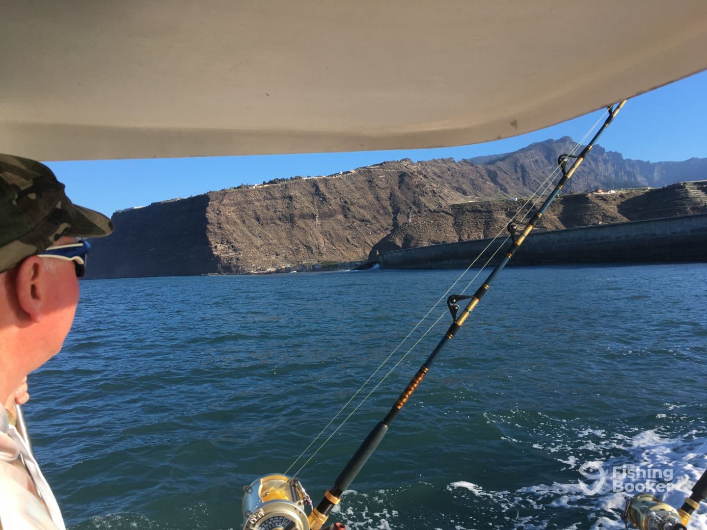 A fisherman enjoying the scenic view of rugged cliffs while aboard a fishing boat, with fishing gear visible in the foreground.