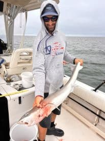 Angler displaying a freshly caught shark on a fishing charter, showcasing the excitement of deep-sea fishing.