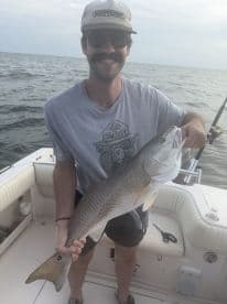 An angler proudly displaying a large Redfish while aboard a fishing boat, showcasing a successful day on the water.