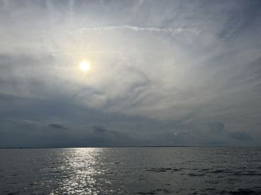 A serene view of the water reflecting the sun, with a cloudy sky overhead, capturing the tranquil atmosphere of a fishing environment.