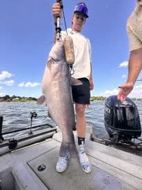 A young angler proudly displaying a large Catfish while fishing on a boat, showcasing the excitement of a successful catch.