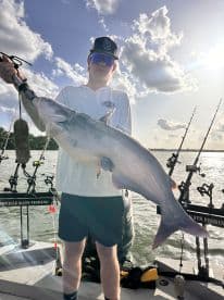 A young angler proudly displaying a large catfish while fishing on a boat, showcasing a sunny day on the water.