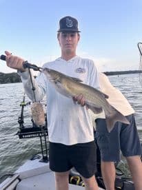 Young angler proudly holding a Catfish while fishing on a boat, showcasing a successful catch during a lake outing.