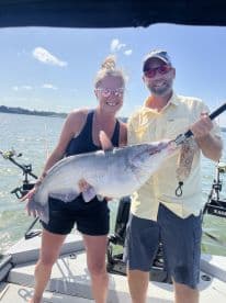 Two anglers proudly displaying a large Catfish aboard a fishing boat, enjoying a sunny day on the water.