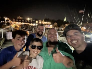 Group of four individuals posing for a photo at night near a marina, with boats in the background.