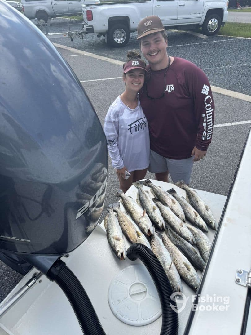 A couple proudly displaying their catch of speckled trout on a boat after a successful fishing trip.