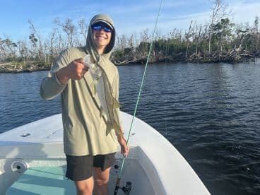 Angler holding a Snook while fishing from a boat in a scenic waterway, showcasing a successful catch.