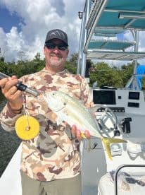 An angler proudly displaying a Yellowtail Snapper aboard a fishing boat in a scenic coastal environment.
